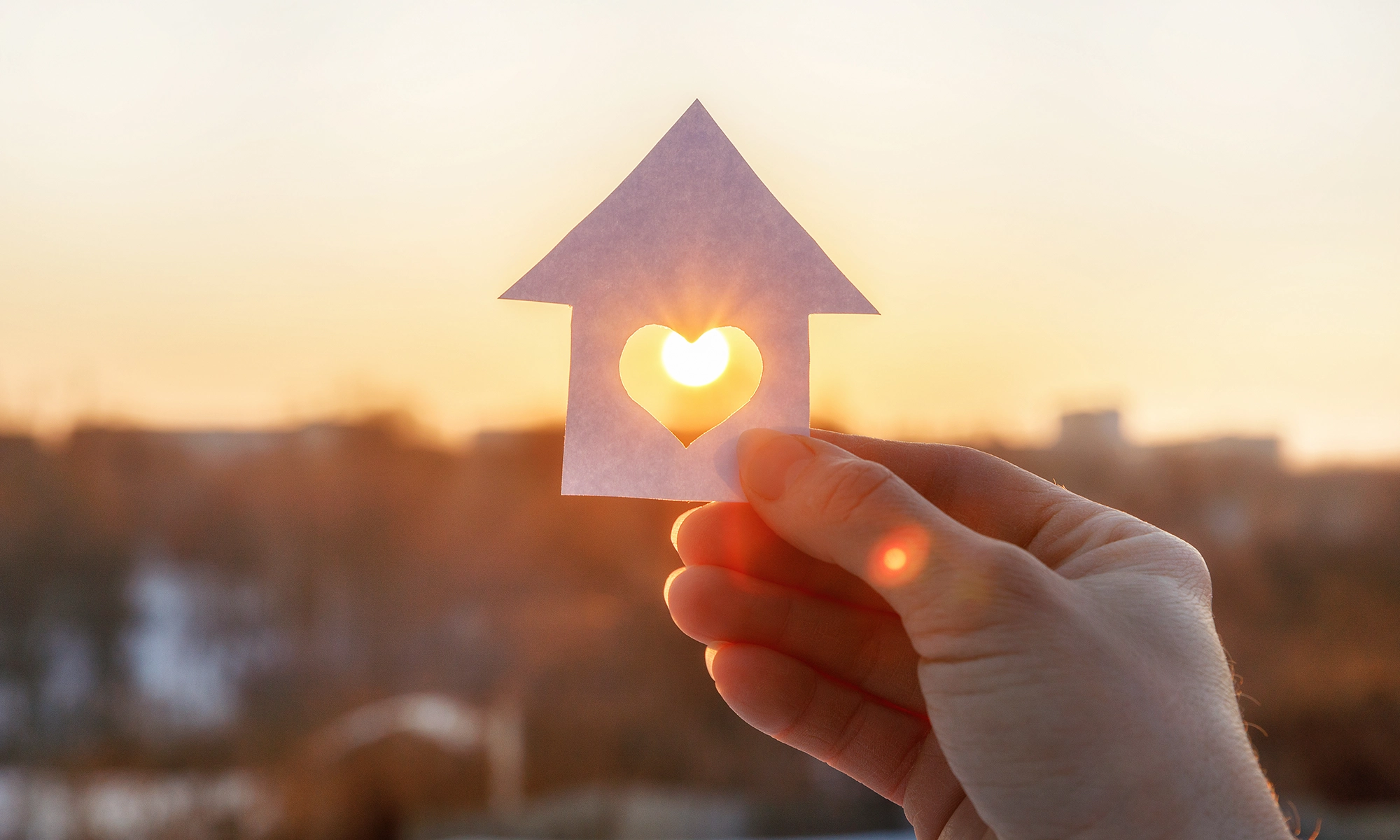 hand holding paper cut out of house up to the sunrise