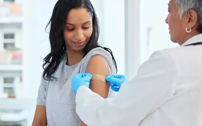 Doctor applying a bandage to a woman's arm after receiving a vaccine.