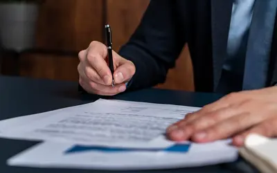 A person in a business suit signing a document on a desk
