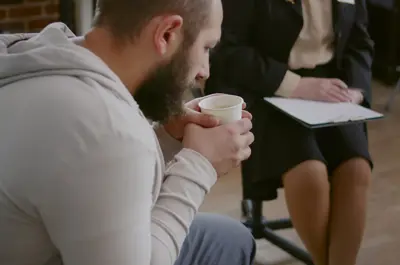 Close up of man trembling while drinking cup of coffee at a group meeting with a counsellor.