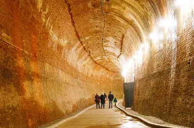 An old water outlet tunnel from the power station has been converted to a hike to the foot of Niagara Falls. A family walks through the tunnel, which has a very high ceiling.