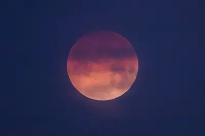 The moon is multiple shades of orange and covered in shadow during a Blood Moon coinciding with a total lunar eclipse