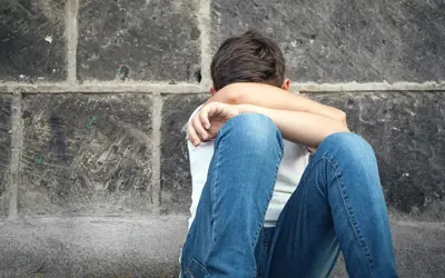 Boy sitting against a wall with his head down and resting on his arms
