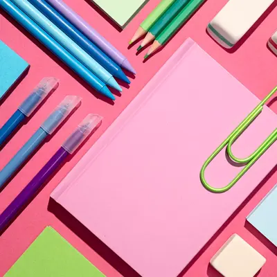 Colourful pens, pencils and paper on a pink background