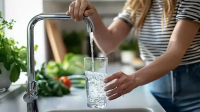 Woman filling a glass with water from the tap in her kitchen
